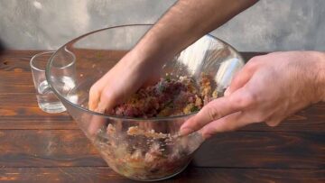 A hand mixing the meat mixture in a bowl.