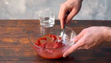 A hand mixing the tomato sauce with a spoon.