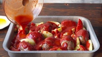 Adding the tomato sauce over the potatoes and the patties.