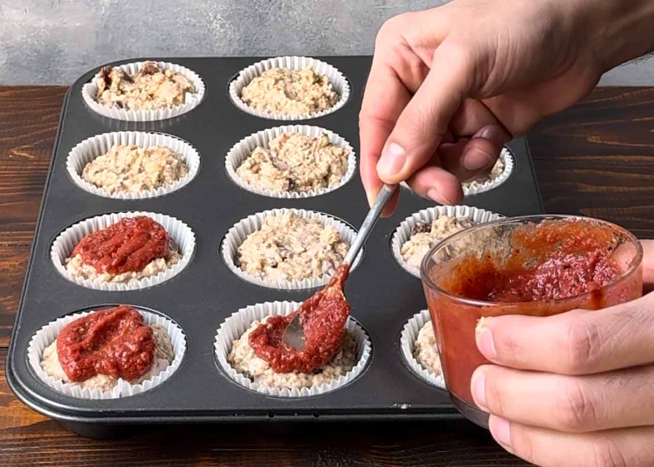 Adding the pizza sauce over the muffins.
