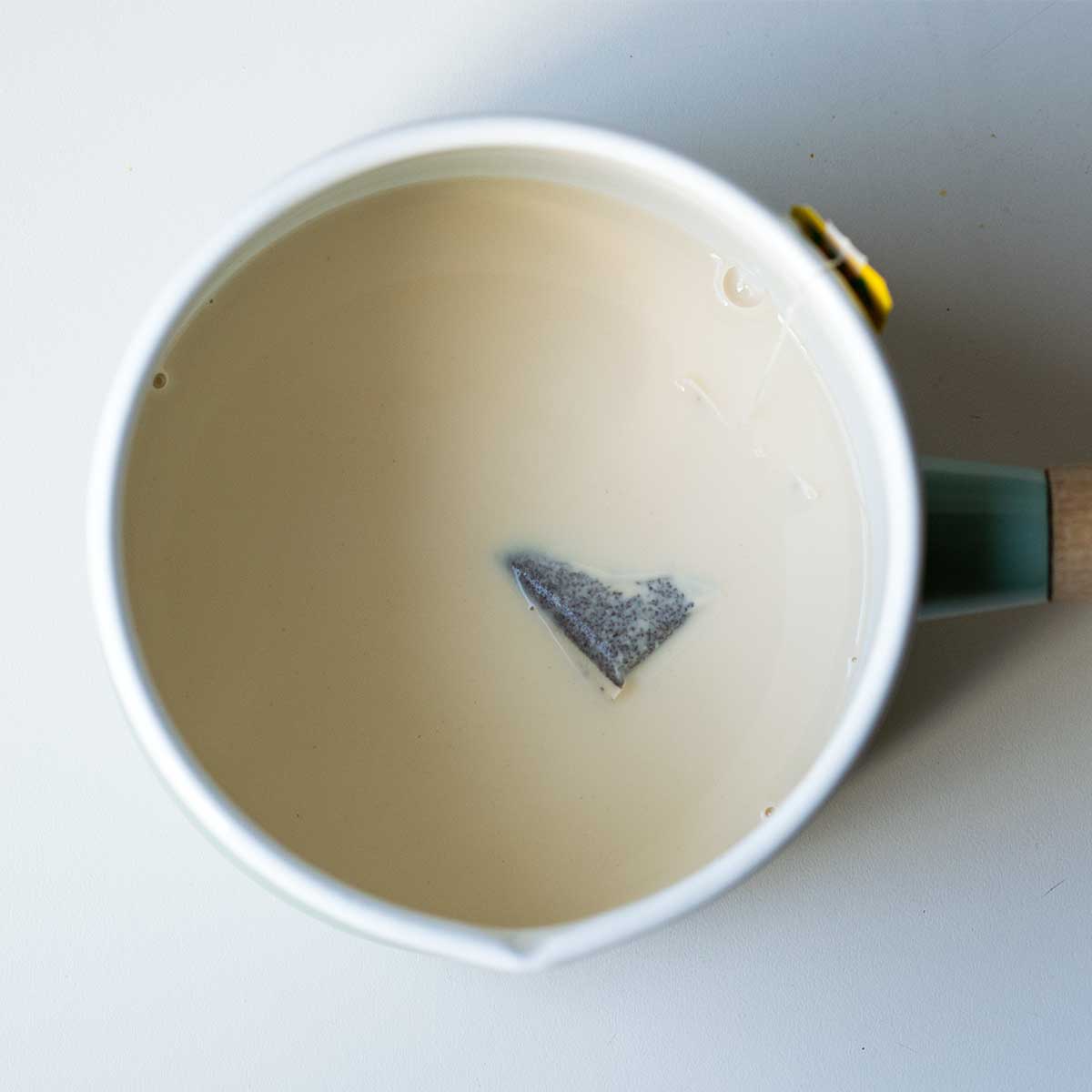 Steeping the black tea bag in the hot milk inside a saucepan.