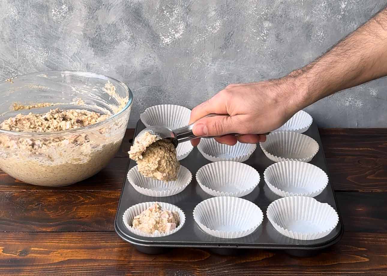 A hand scooping the muffin batter into the holes of a muffin tin.
