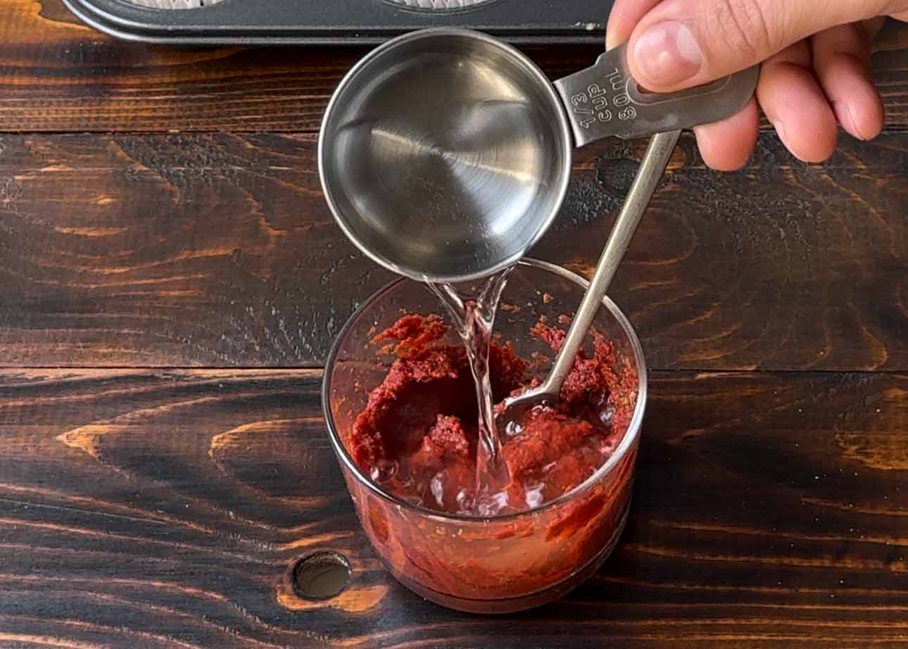 A hand adding water to tomato paste.