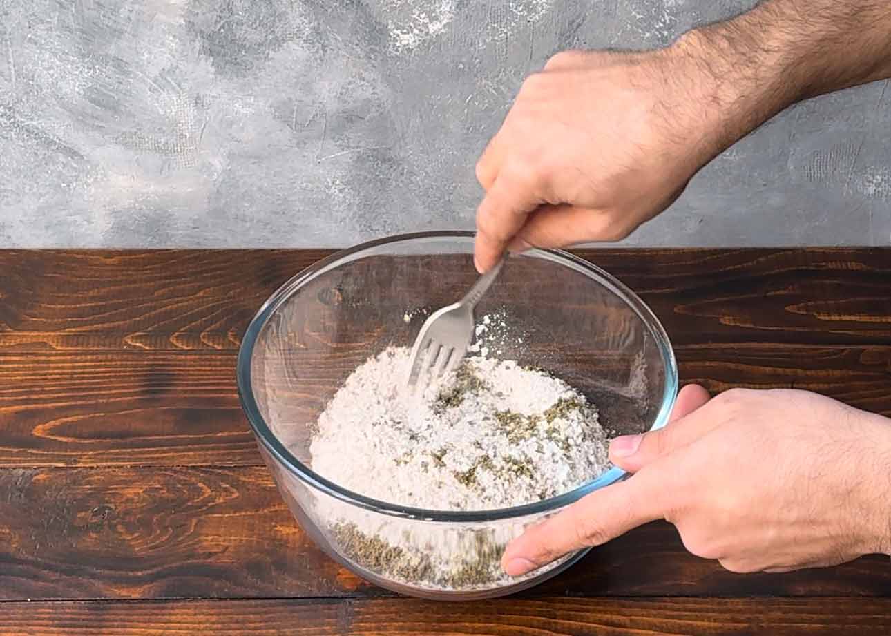 A hand mixing the dry ingredients in a bowl.