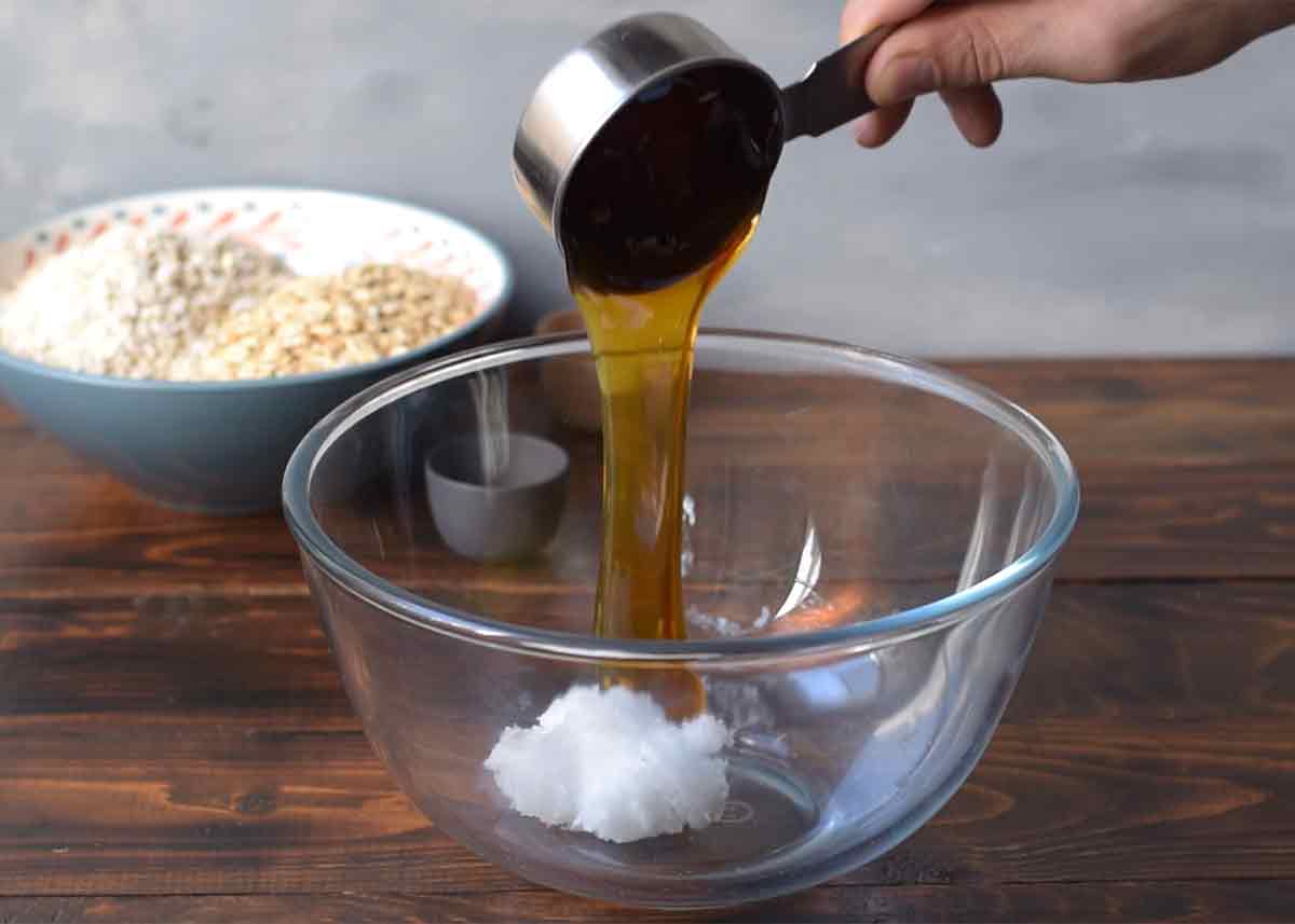A hand adding honey to a bowl with coconut oil.