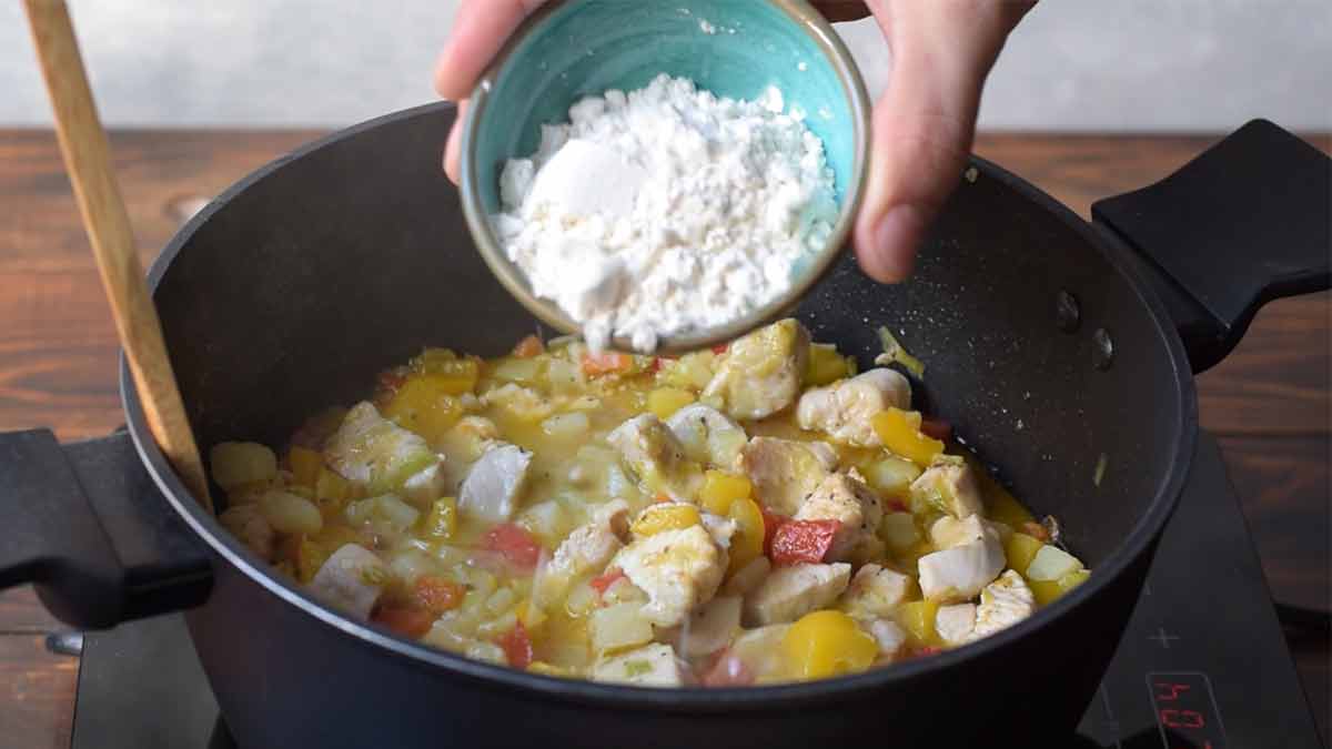 A hand sprinkling flour over the chicken and veggies in the pot.