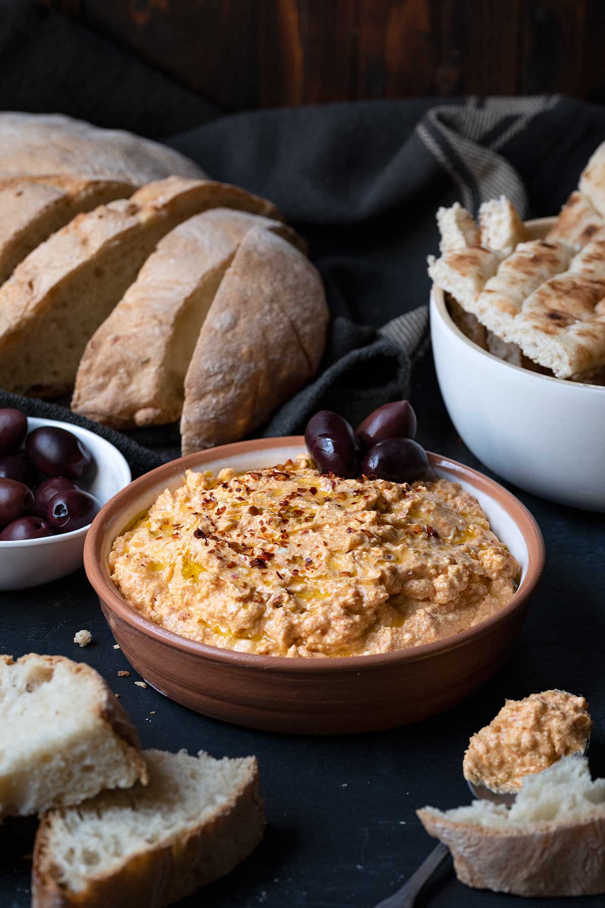 Slices of fresh bread, and a bowl with tirokafteri with a used spoon next to it.