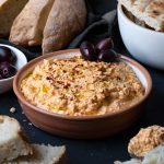 Greek spicy feta dip served in a bowl with pita bread and Kalamata olives.