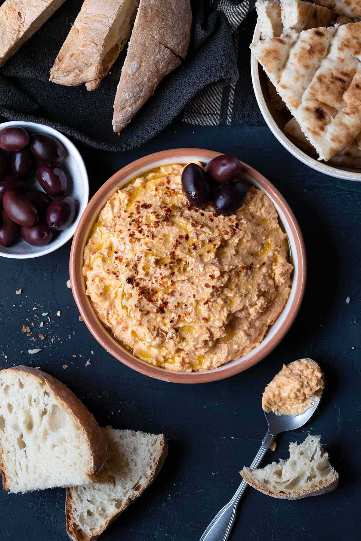 A plate with tirokafteri served with fresh bread, pita bread and Kalamata olives.