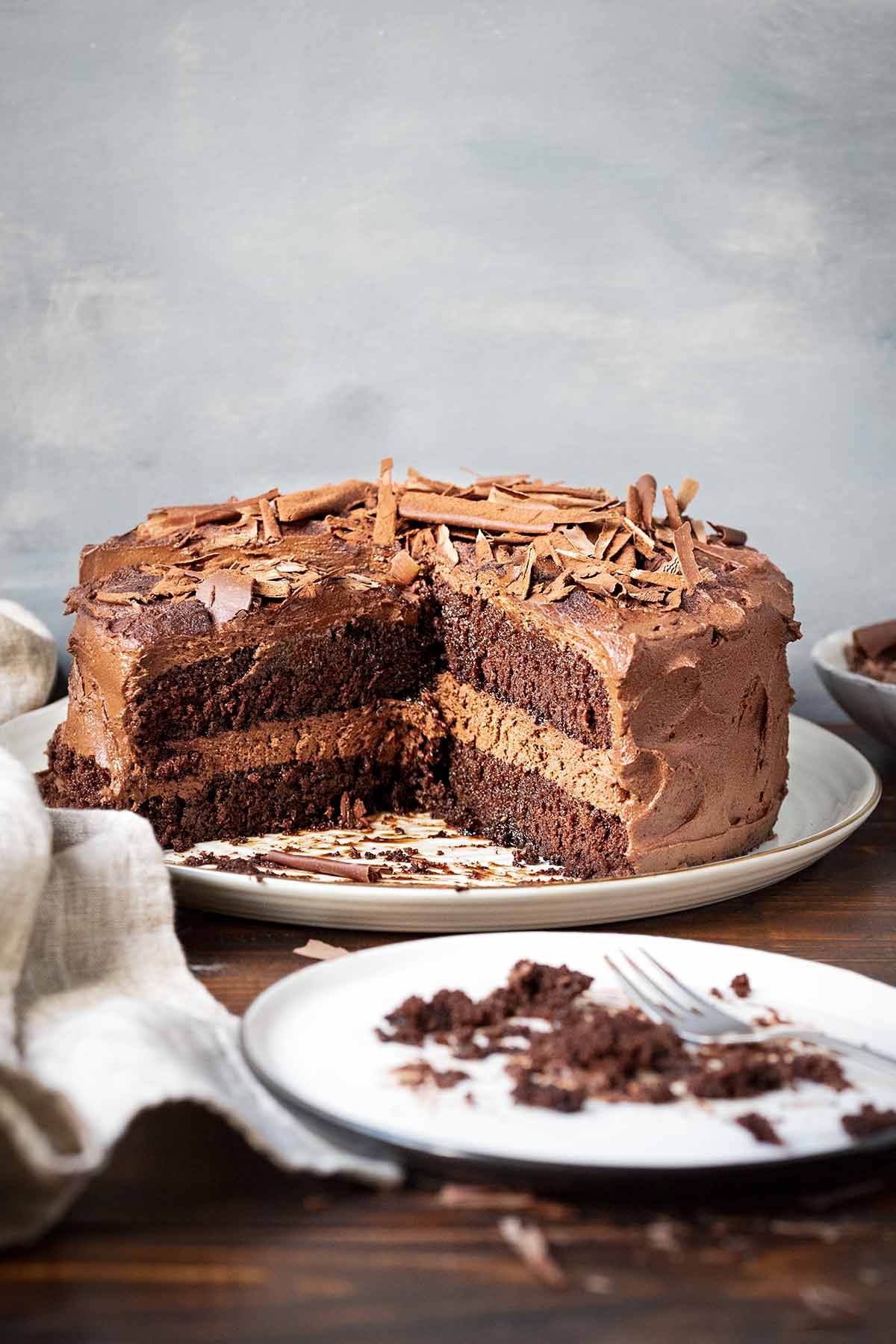 A cut chocolate cake on a serving platter and an empty plate with cake crumbs.