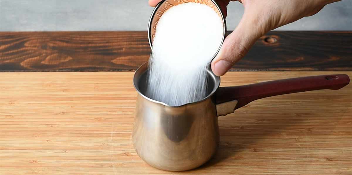 A hand pouring sugar into a small pot.