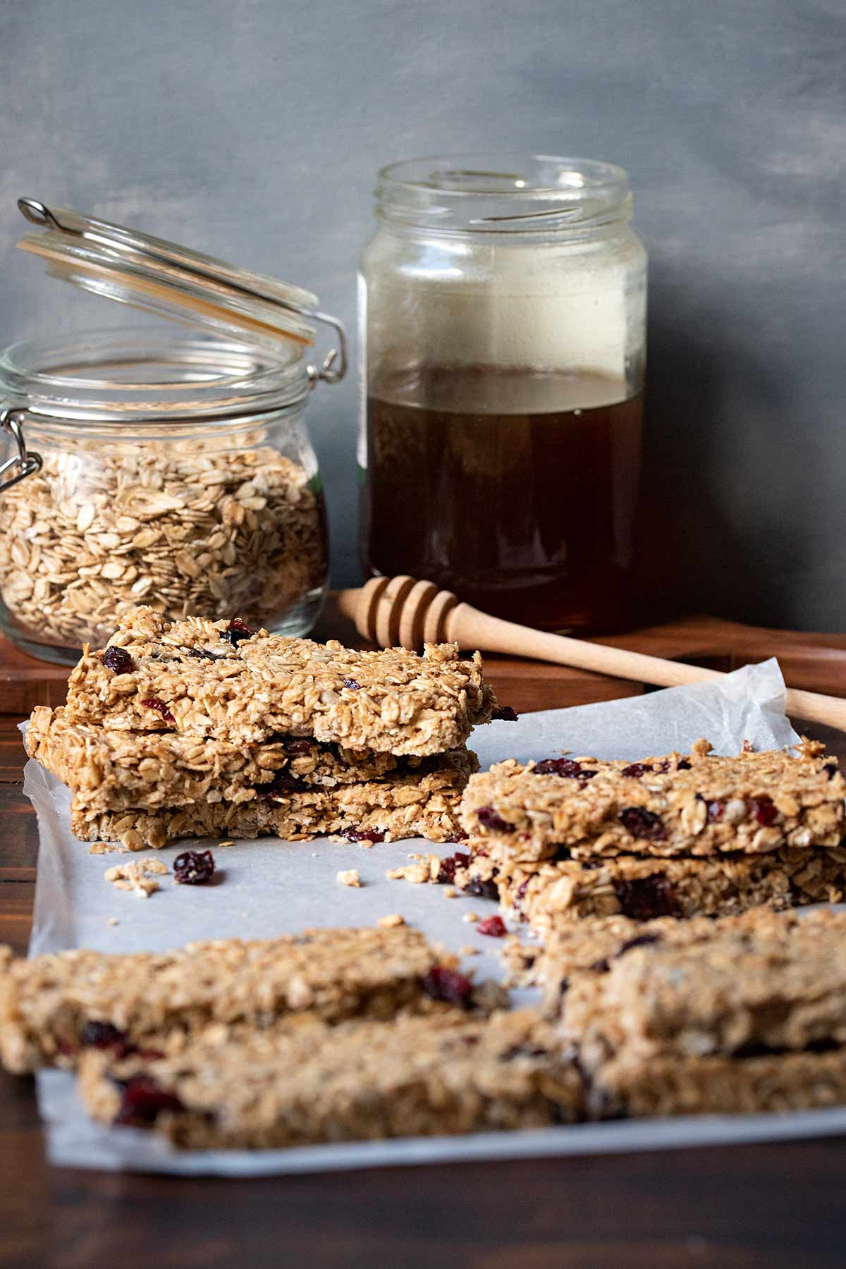 Baked oatmeal bars on parchment paper next to a jar with oat and a jar with honey.