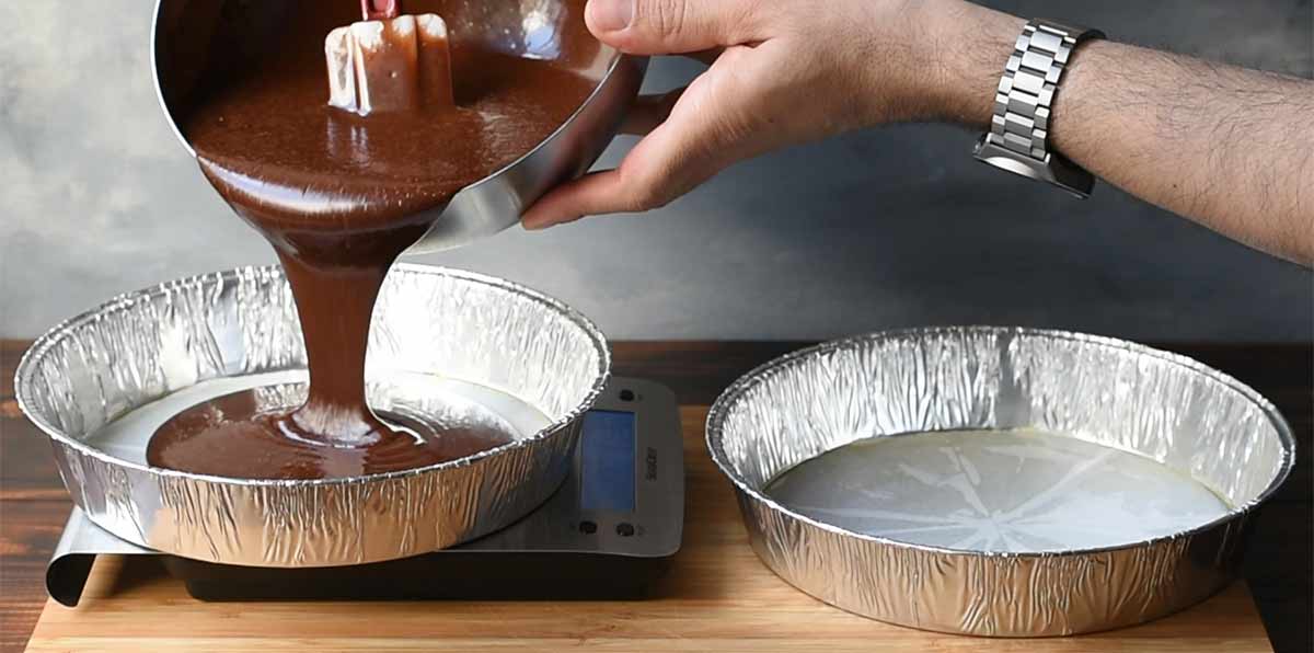 Two hands pouring the cake batter into the prepared pans.