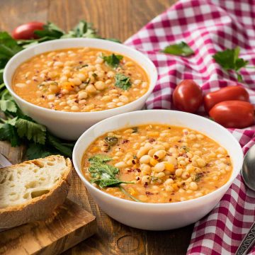 Two bowls of Italian white bean soup, fresh bread on a cutting board and a towel.