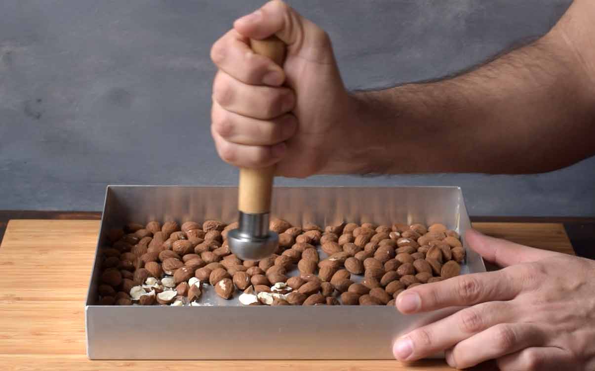 A hand smashing roasted almonds with a pestle.