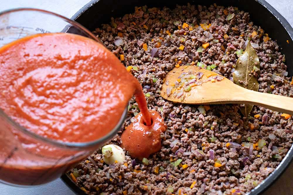 Process shot showing how to add pureed tomatoes.