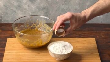 A hand adding baking soda to a bowl with flour.