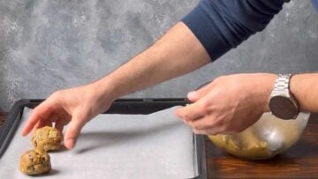 A hand placing cookie balls onto a baking sheet lined with parchment paper.