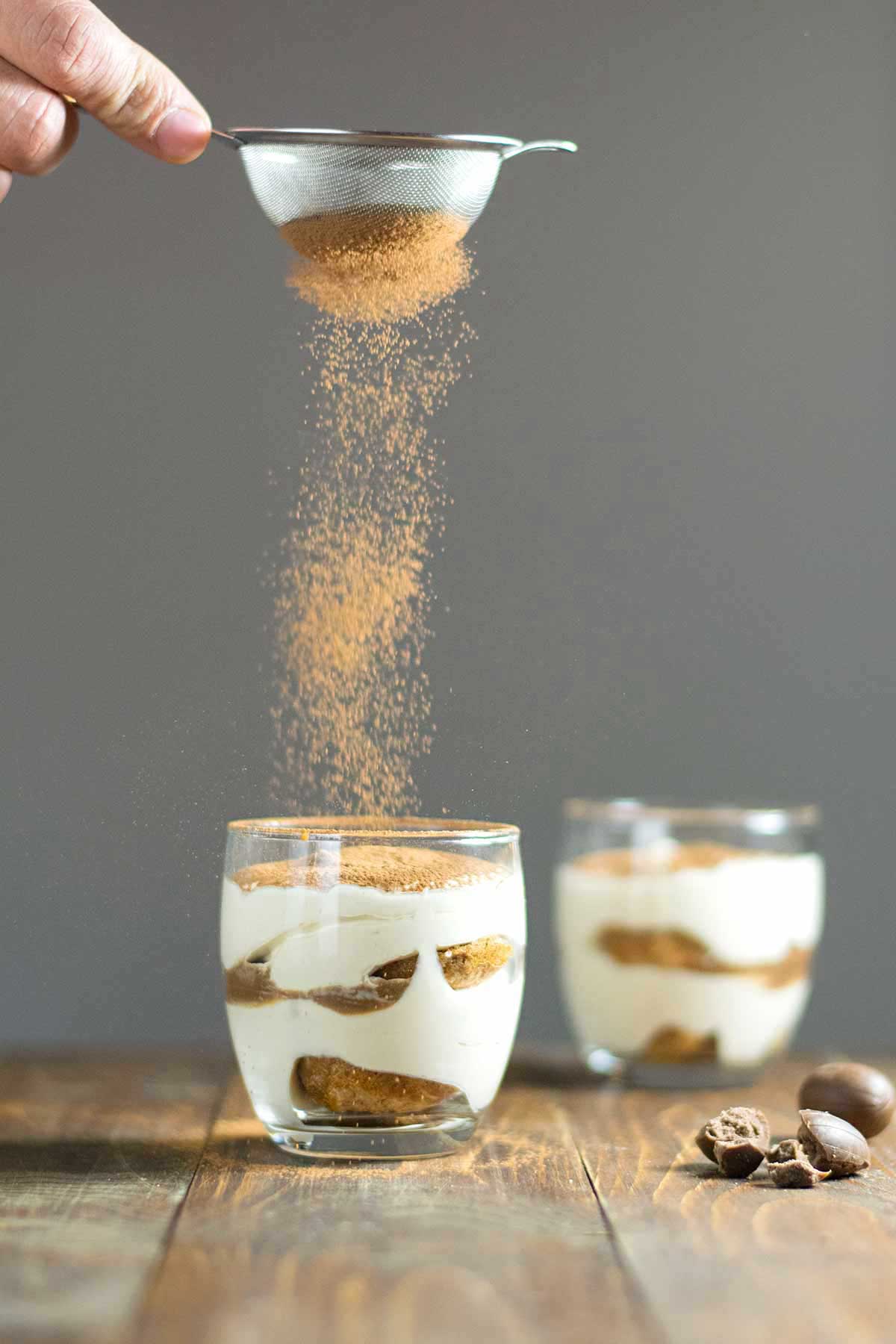 Eggless Tiramisou in cups being dusted with cocoa powder.
