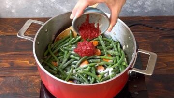 Adding tomato paste to a pot with green beans.