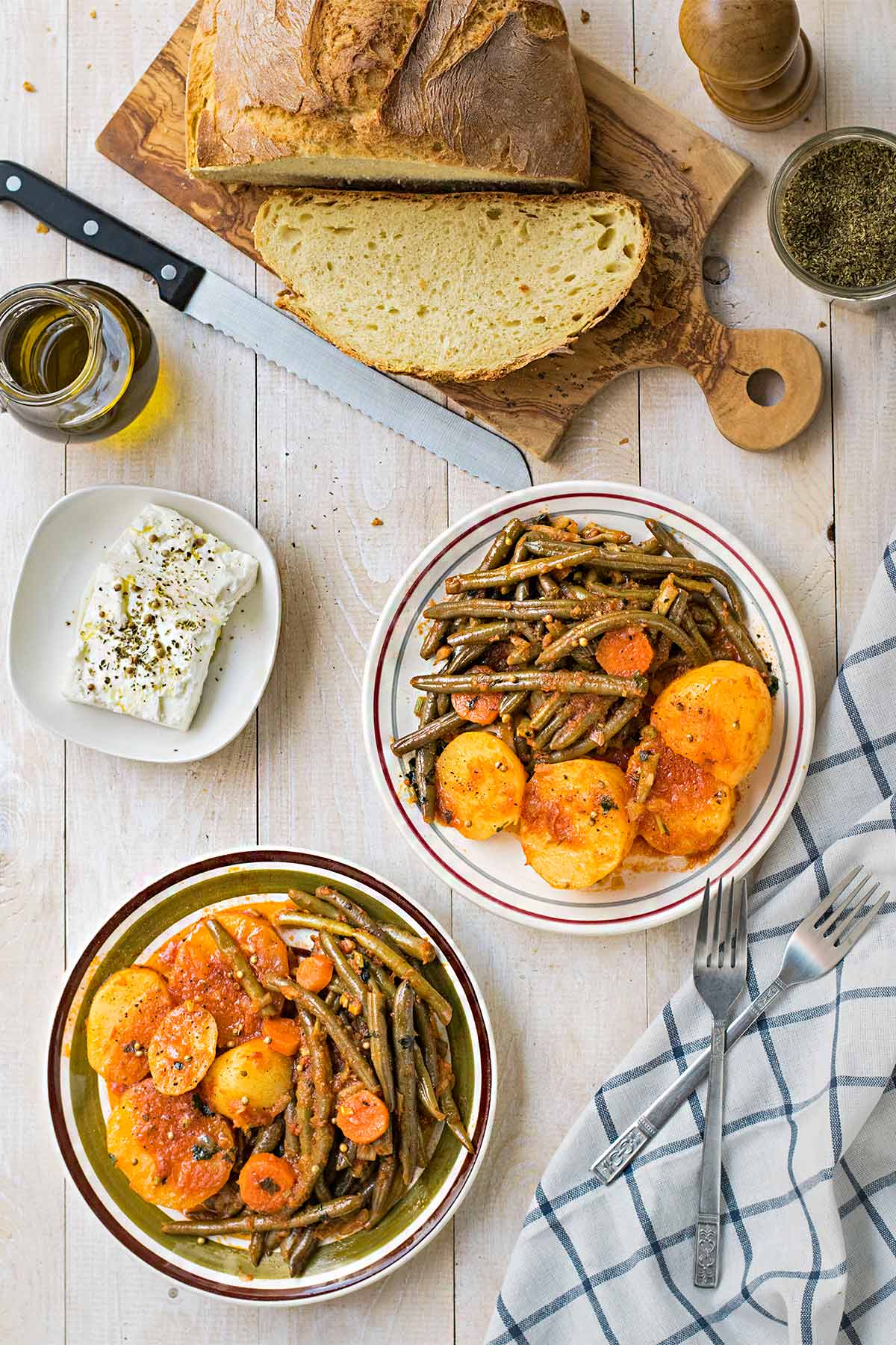 Greek green bean stew with potatoes served on plates with bread and feta cheese.