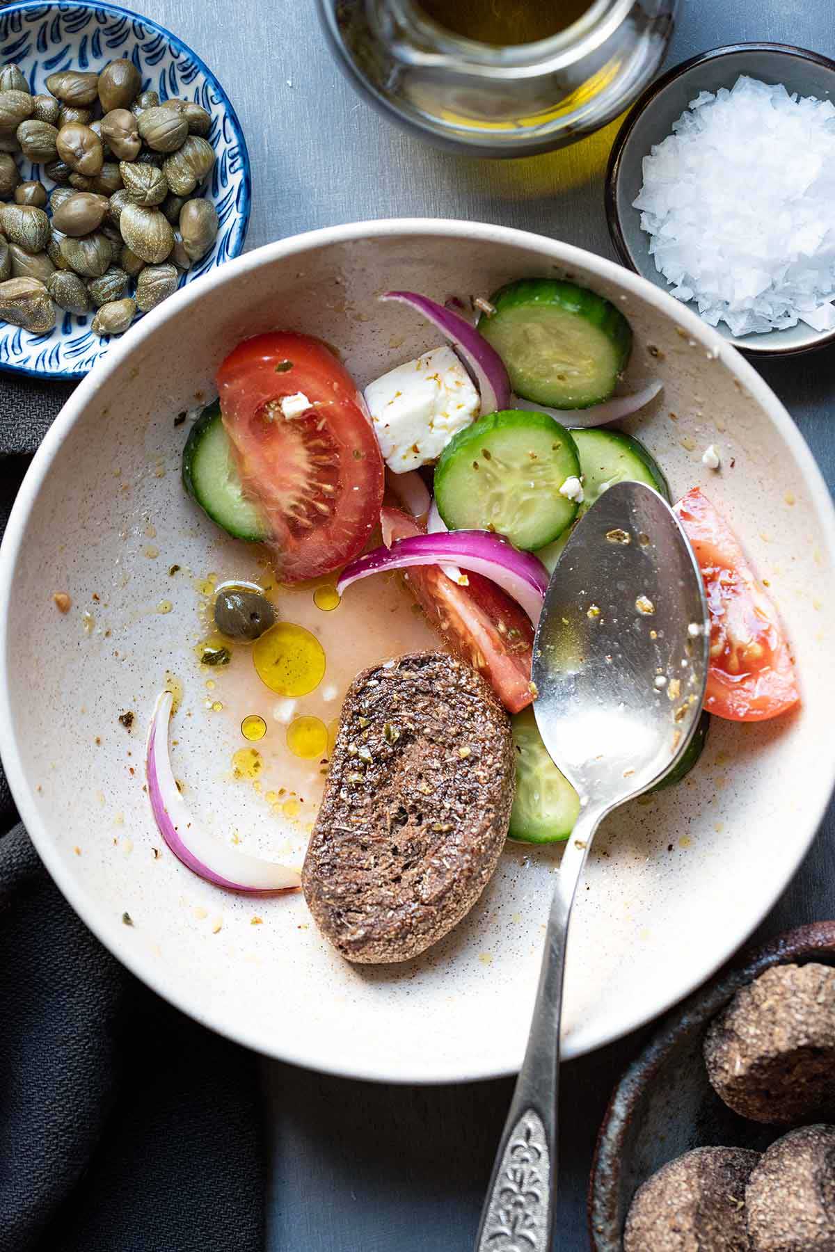 Half-eaten Greek salad with feta, with a barley rusk soaked in the juices.