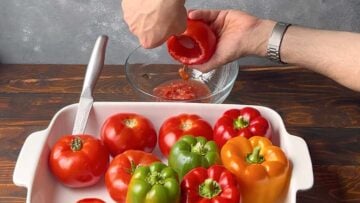 A hand hollowing a tomato with a spoon.
