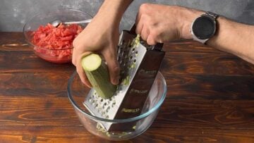 A hand grating a zucchini through a box grater.