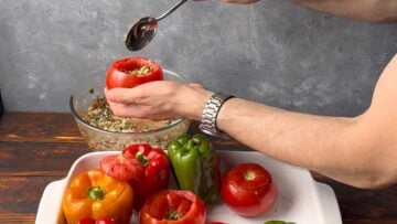 A hand filling a tomato with the rice mixture.