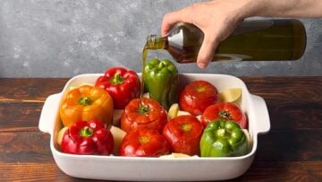 A hand drizzling the vegetables with olive oil.