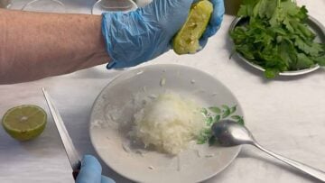 A hand squeezing lemon over grated onion.
