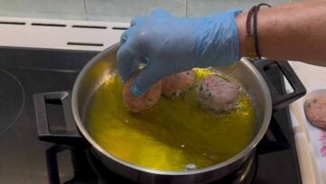A hand adding meatballs to a frying pan with oil.