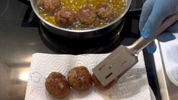 A hand transferring keftedes from the pan to a plate.