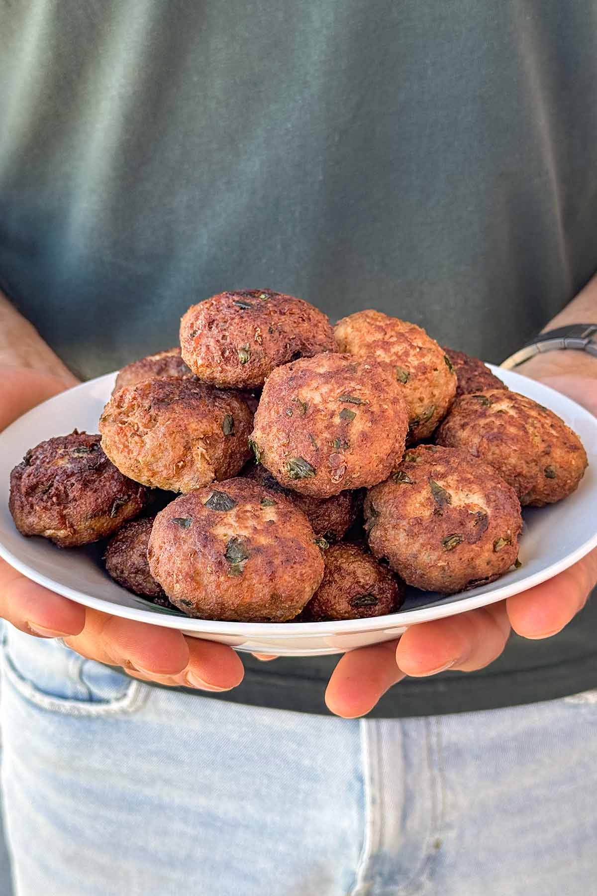 A guy holding a plate with keftedes.