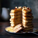 A stack of whole wheat apple pancakes with maple syrup.