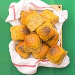 Pumpkin dinner rolls inside a wooden basket.