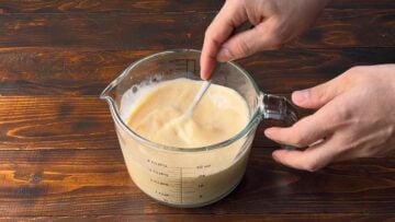 A hand mixes the ingredients for the custard in a bowl.