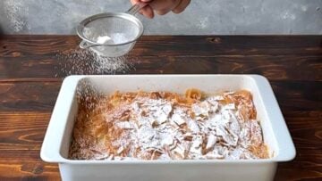 A hand sprinkling icing sugar the easy bougatsa.