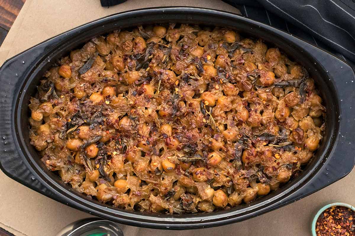 Baked chickpeas with a layer of caramelized onions on top inside a deep baking dish.