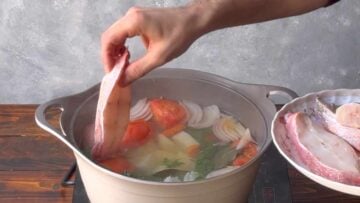 A hand adds fish to the pot.