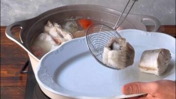 A hand removes the fish from the pot with a slotted spoon.