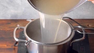 A hand passing the fish stock through a strainer.