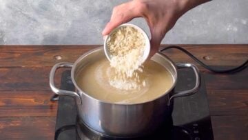 A hand adding rice to the fish soup.