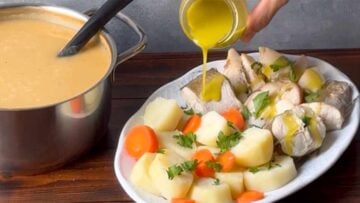 A hand pouring ladolemono sauce over the fish and potatoes.