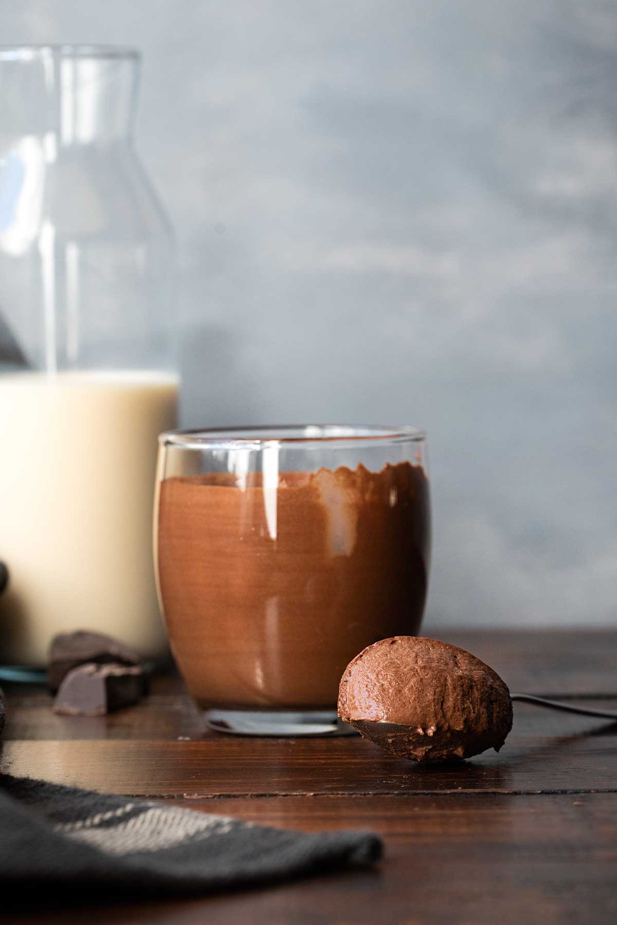 A glass with 2-ingredient chocolate mousse, a spoon and a bottle of milk.
