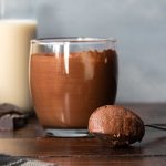 A glass with 2-ingredient chocolate mousse, a spoon and a bottle of milk.