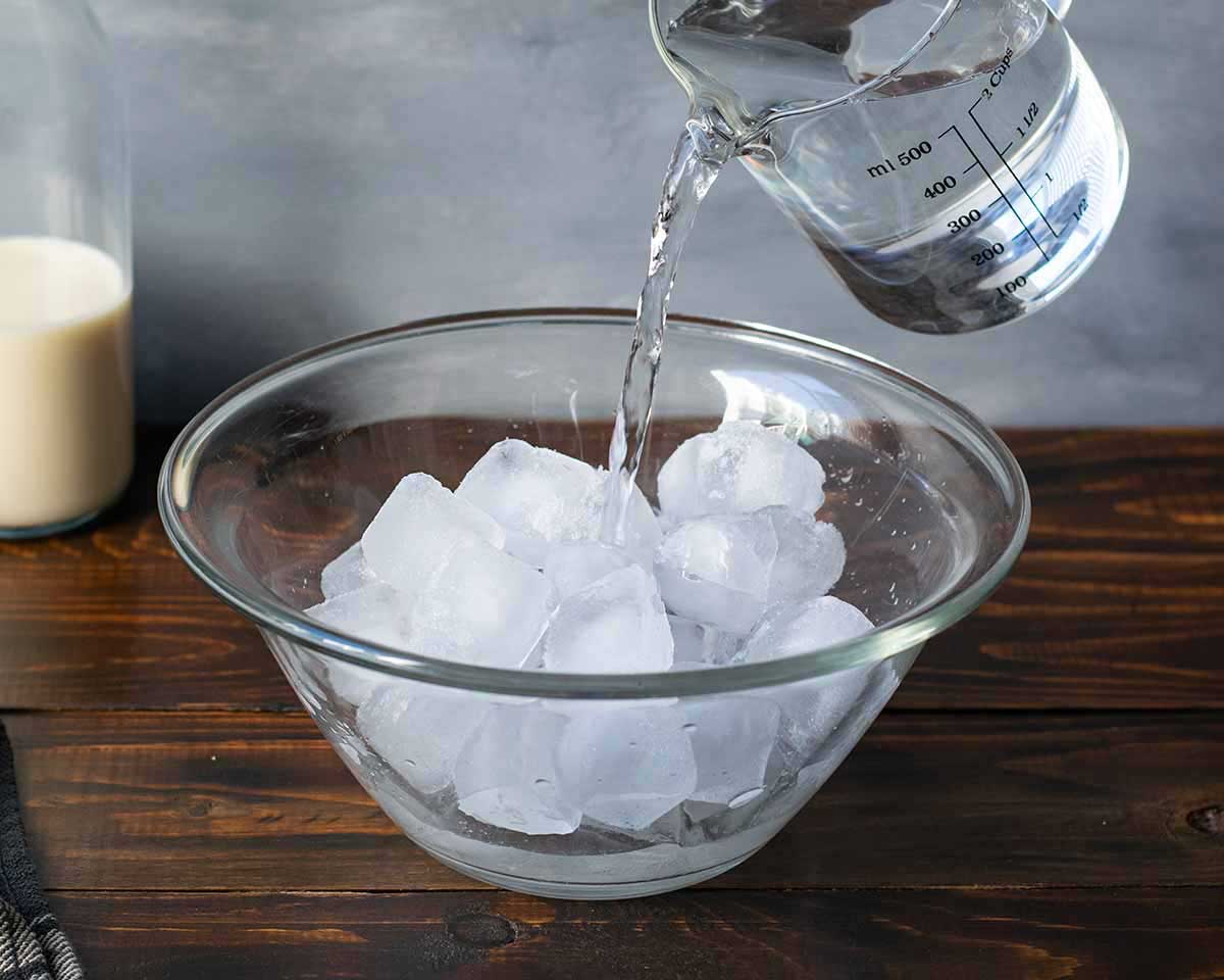 A bowl with ice cubes being filled with cold water (ice bath).