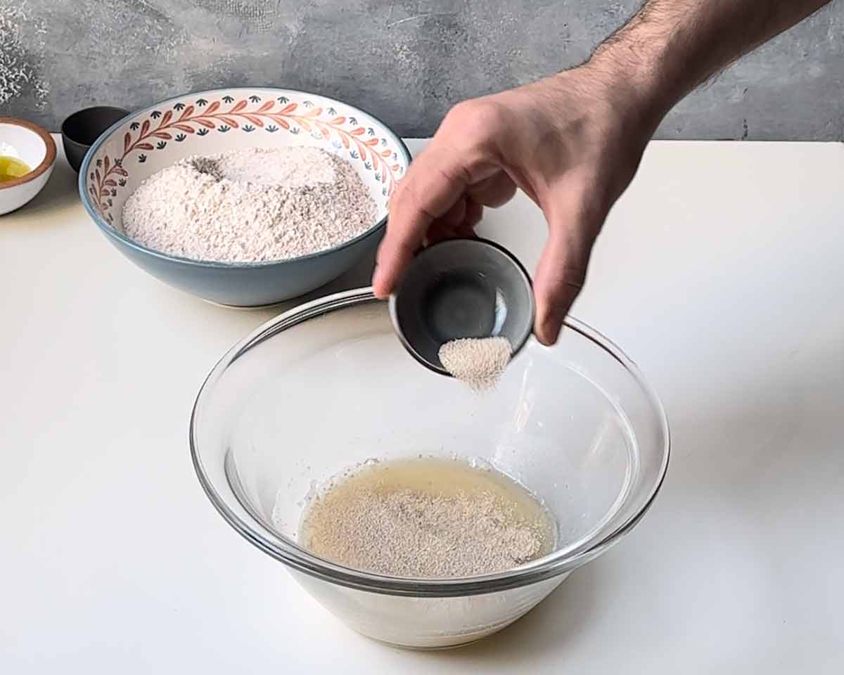 A hand sprinkling dry yeast over warm water.