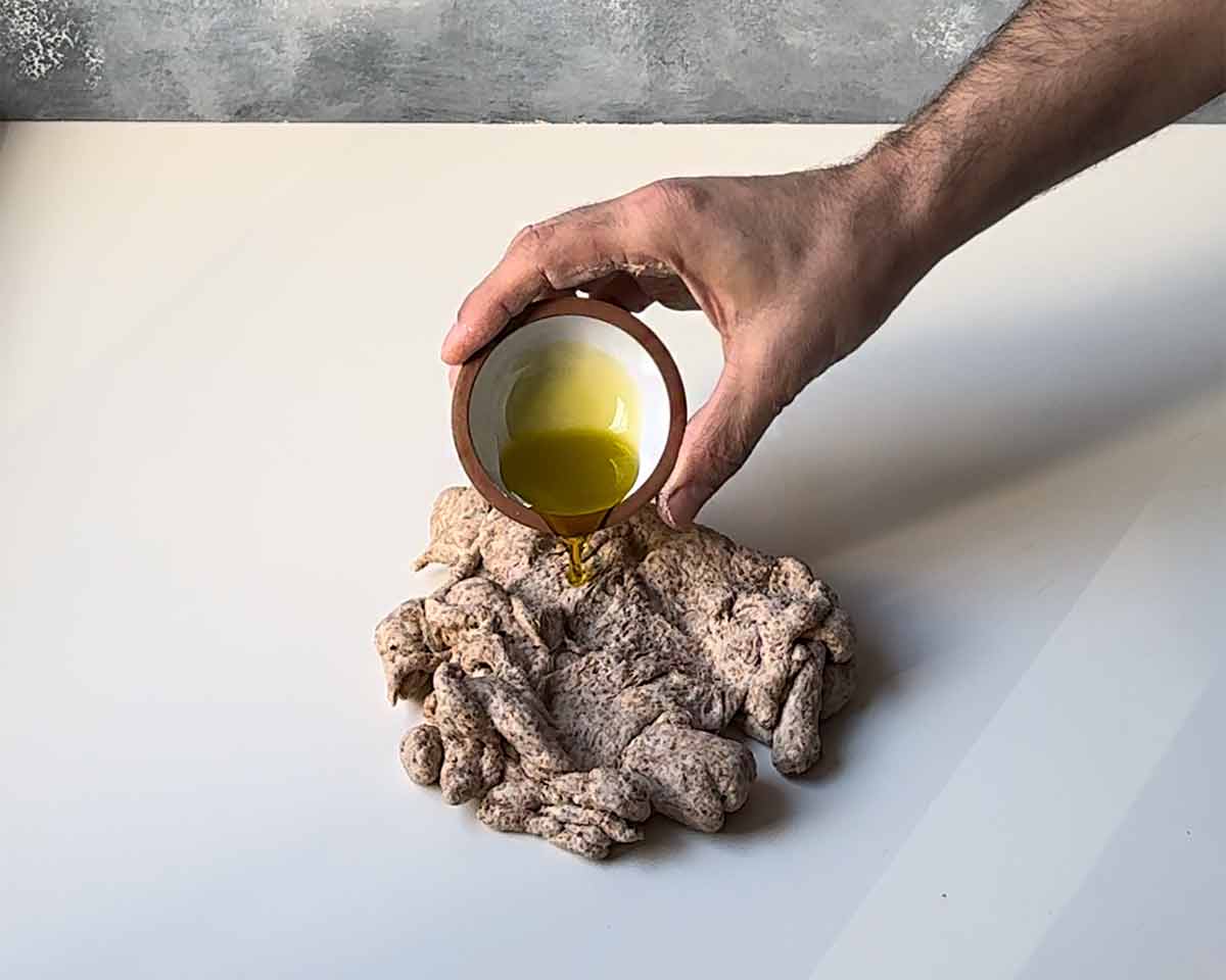 A hand adding olive oil to the bread dough.