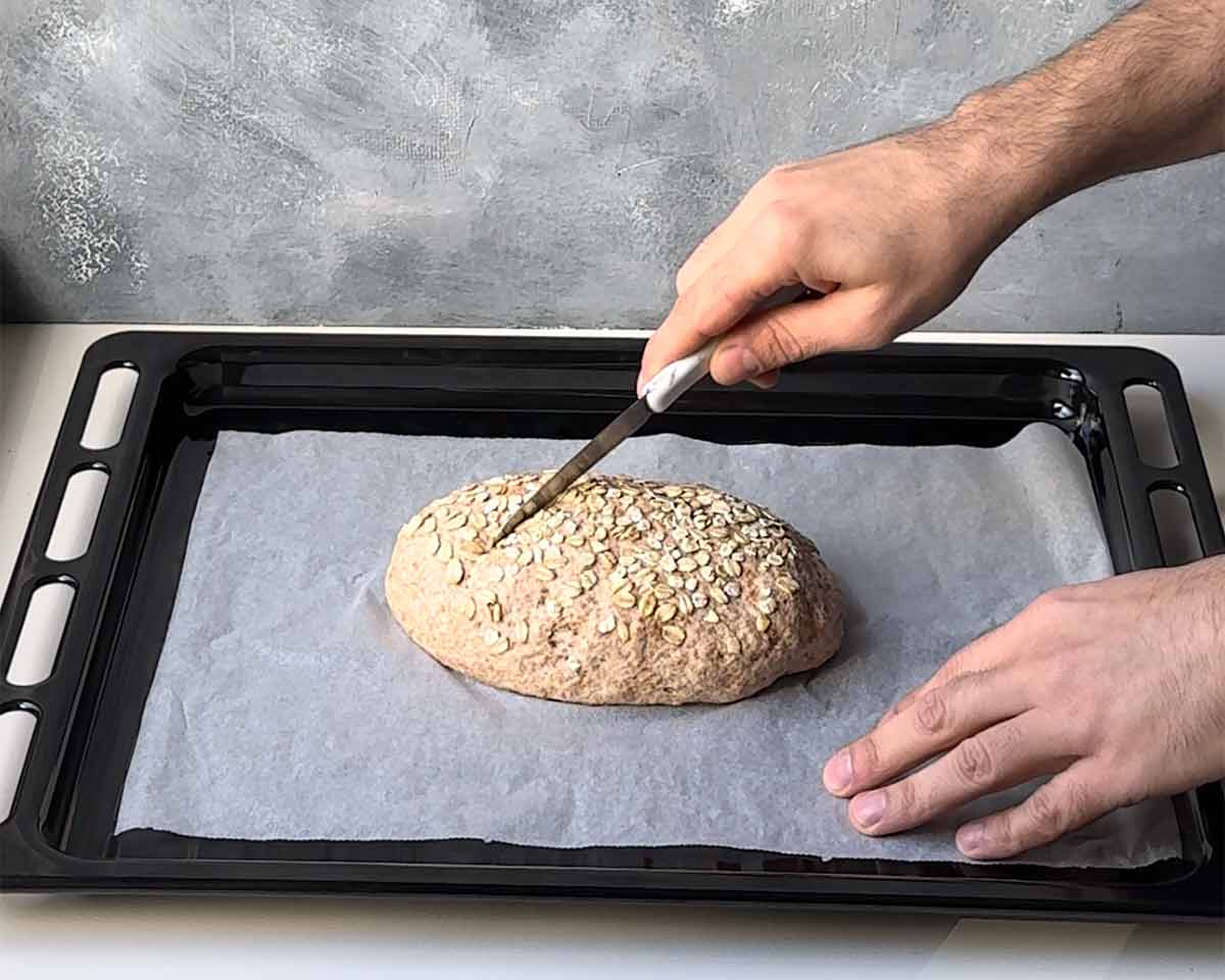 A hand scoring the loaf with a knife before baking.